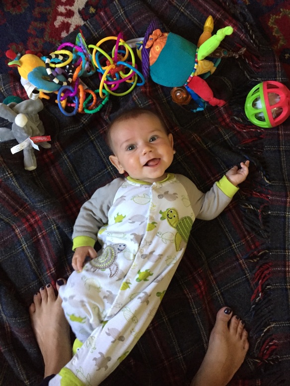 A baby on the ground, surrounded by toys and smiling